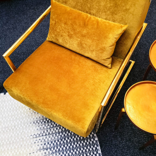 Dark yellow velvet armchair and golden side table. Modern furniture with retro feel.